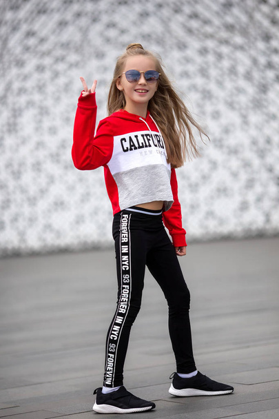 Little girl in a tracksuit is dancing modern dance on the street. Young urban hip hop dancer - Photo, Image