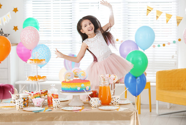 Happy girl at table with treats in room decorated for birthday party - Photo, image