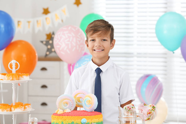 Happy boy at table with treats in room decorated for birthday party - Фото, изображение