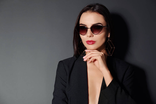Beautiful woman wearing jacket and sunglasses on black background, space for text - Fotografie, Obrázek
