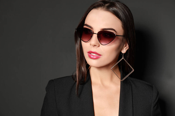 Beautiful woman wearing jacket and sunglasses on black background - Foto, afbeelding