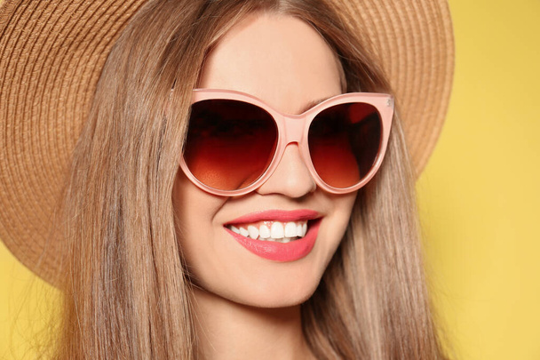 Young woman wearing stylish sunglasses and hat on yellow background - Foto, imagen