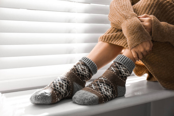 Woman wearing knitted socks on window sill indoors, closeup. Warm clothes - Valokuva, kuva