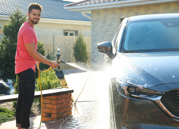 Young happy man washing car at backyard on sunny day - Foto, afbeelding