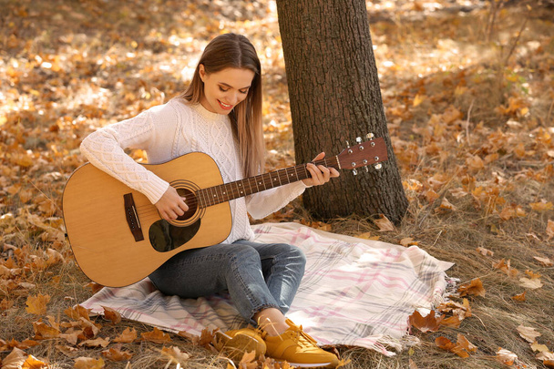 Teen girl playing guitar in autumn park - 写真・画像