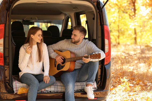 Young couple with guitar sitting in open car trunk outdoors - Photo, image