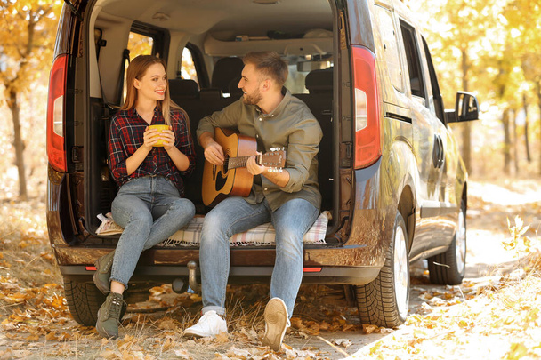 Young couple with guitar sitting in open car trunk outdoors - Фото, зображення