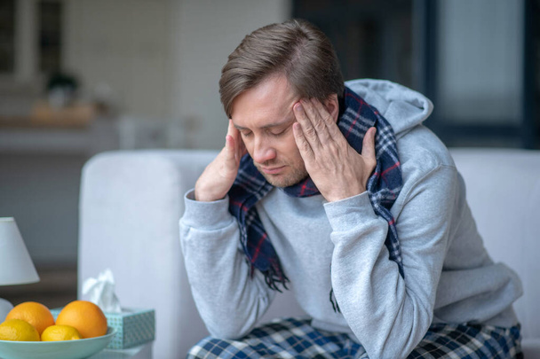Donkerharige man draagt een geruite sjaal voelt zich slecht met hoofdpijn - Foto, afbeelding