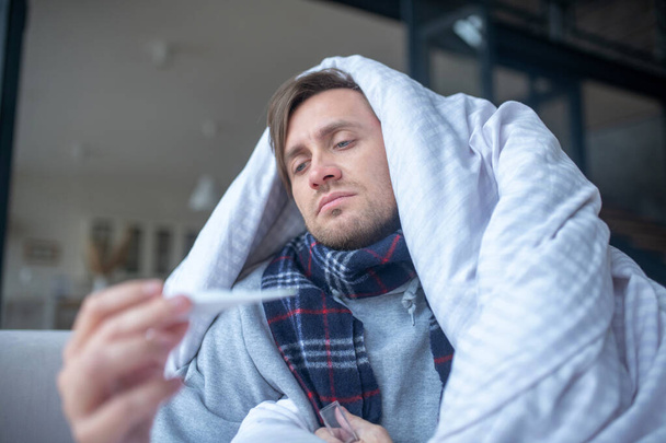 Sick man wearing warm scarf measuring temperature - Foto, Imagem