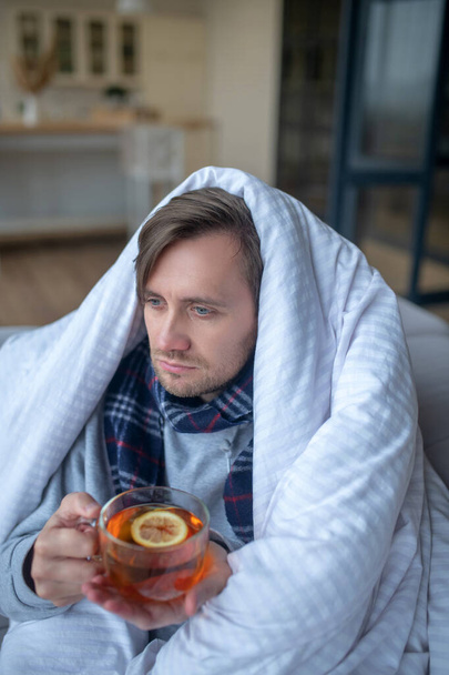 Top view of sick blue-eyed man drinking tea with lemon - Foto, Imagem