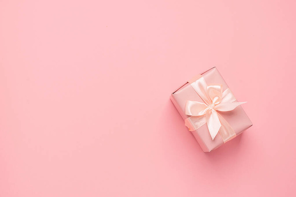Festive gift box with satin ribbon bow on a pastel pink background. Festive minimalism concept. Flat style layout. - Photo, Image