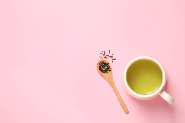Spoon with green tea leaves and cup of hot beverage on pink background, flat lay. Space for text - Fotó, kép