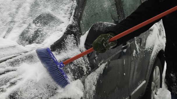 Az autó oldalának megtisztítása a hótól az ecsettel. - Fotó, kép