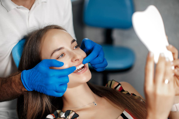 Dental clinic. Reception, examination of the patient. Teeth care. Young woman undergoes a dental examination by a dentist.Happy patient and dentist concept.Male dentist in dental office talking with girl patient.Beautiful teeth - Foto, Imagem