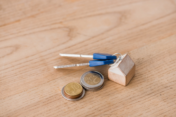 κλειδιά με μπιχλιμπίδι σπίτι παιχνίδι κοντά σε χρυσά και ασημένια νομίσματα σε ξύλινο τραπέζι - Φωτογραφία, εικόνα