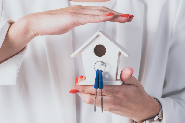cropped view of businesswoman holding and covering house model and keys with hand - Photo, Image