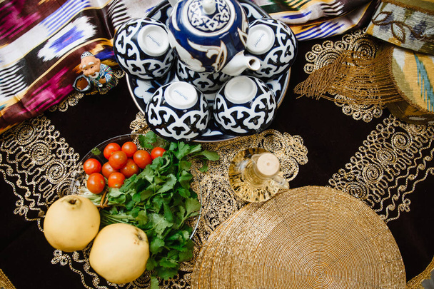 Quince fruit op een tafel versierd met oosterse stoffen met ornamenten en gouden accenten. Het concept van oosterse gerechten. Quince fruit, tomaten en kruiden staan op tafel - Foto, afbeelding