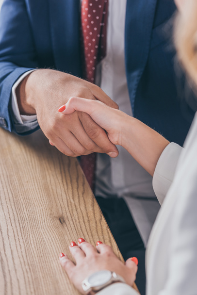 cropped view of businessman shaking hands with woman while sitting at wooden desk - Photo, Image