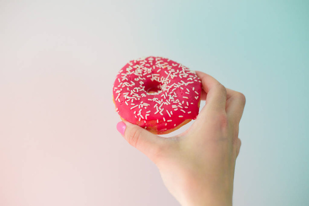 Рожевий пончик в руці, барвистий фон
 - Фото, зображення