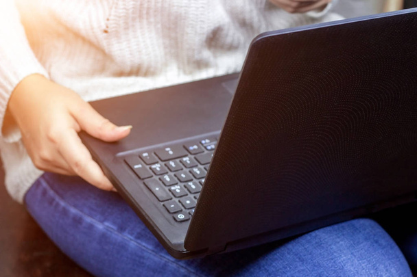 Молода жінка в блакитних джинсах сидить і використовує чорний ноутбук
. - Фото, зображення