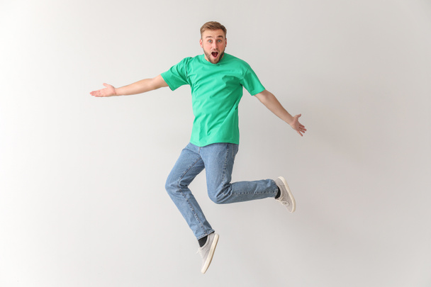 Surprised jumping young man on light background - Foto, imagen