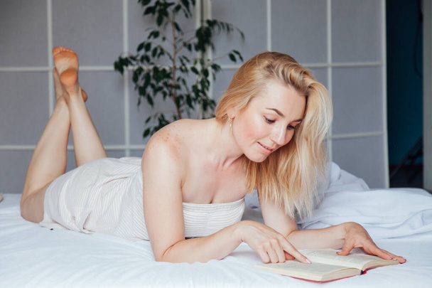Mulher loira bonita lê um livro no quarto na cama
 - Foto, Imagem