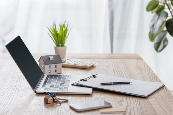bureau en bois avec ordinateur portable, smartphone, clés de maison, presse-papiers avec stylo, modèle de maison et plante verte
 - Photo, image