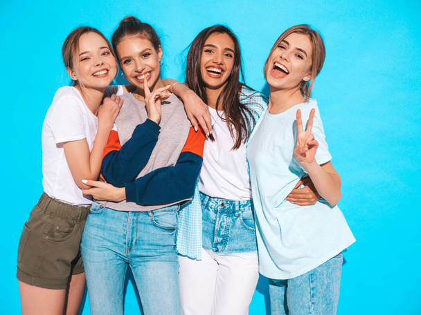 Four young beautiful smiling hipster girls in trendy summer clothes. Sexy carefree women posing near blue wall in studio. Positive models having fun and hugging - Fotoğraf, Görsel