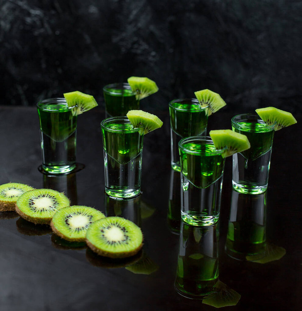 six glasses of kiwi shots in dark background with kiwi slices - Foto, Bild