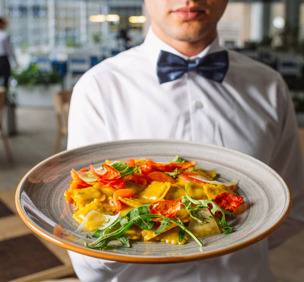 waiter holding a big plate of ravioli with arugula leaves, parmesan cheese - Foto, imagen