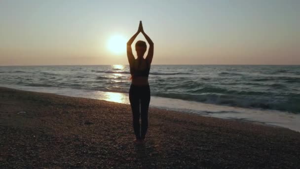 Dziewczyna ćwiczy jogę w pobliżu burzliwego morza. Zwolnij trochę. Tło wschodu słońca - Materiał filmowy, wideo