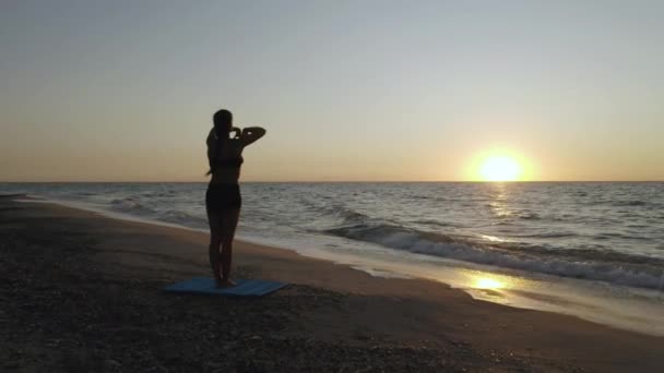 Dívka cvičí jógu u bouřlivého moře. Zpomal. Pozadí východu slunce - Záběry, video