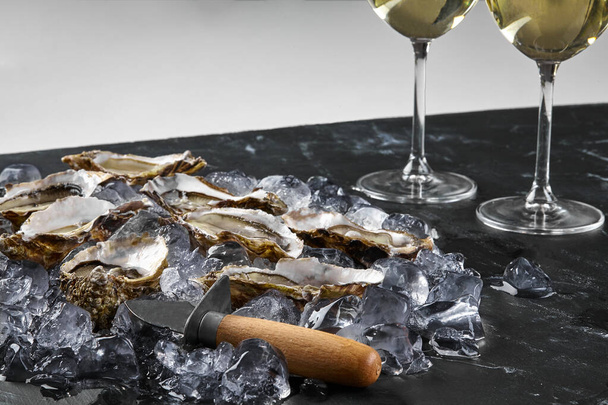 Le ostriche fresche aperte in ghiaccio e champagne sono su un tavolo strutturato in pietra nera. vista con spazio copia. Close-up shot. - Foto, immagini