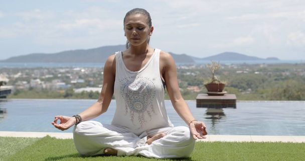 Lady praktiserend yoga in lotushouding tegen oceaankust - Foto, afbeelding