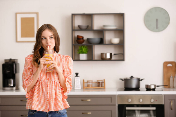 Beautiful young woman drinking orange juice in kitchen - Foto, afbeelding