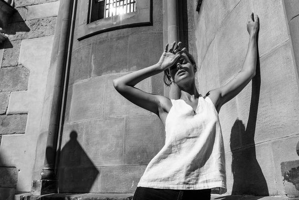 Woman in a white T-shirt standing on the street, shading her face from the sun with shadows. - Foto, Bild