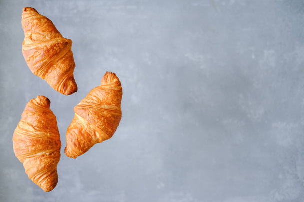 Three freshly baked croissants fly on grey background. Place for text. Creative bakery concept. - Фото, зображення
