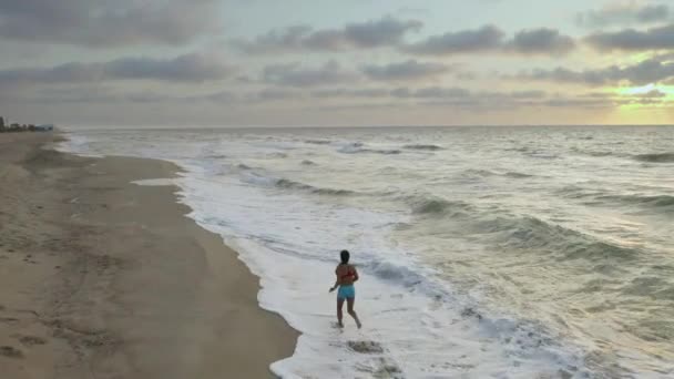 Kadın sabahın erken saatlerinde deniz kıyısında tek başına koşuyor. Gün doğumu - Video, Çekim