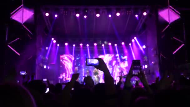コンサートパーティー、携帯電話を手にした群衆の若者たちがステージでの洪水の夜のロックイベントでの記憶のためのライブ音楽とビデオを楽しむ - 映像、動画