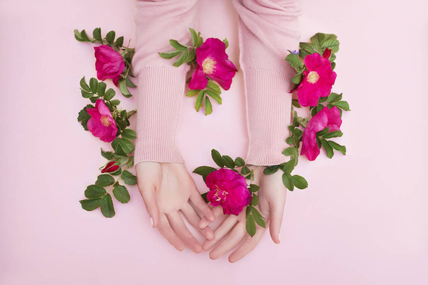 Beauty Hand of a woman with red flowers lies on table, pink pape - Photo, Image