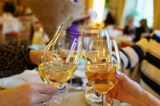 Weingläser mit Weißwein in einem Restaurant. Menschen klirren in einem Restaurant, das einen Geburtstag feiert, mit Weingläsern. Hände ohne Menschen - Foto, Bild