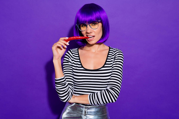 Pretty lady hold red chili pepper in mouth fearless person likes spicy food wear specs striped pullover isolated purple background - Fotografie, Obrázek