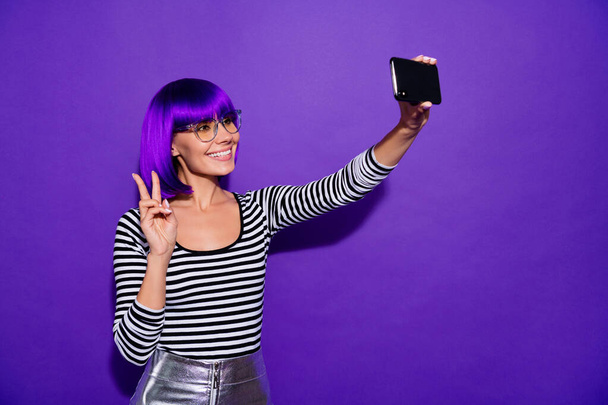 Pretty lady hold hands telephone taking selfies showing v-sign symbol wear specs striped pullover isolated purple background - Photo, image