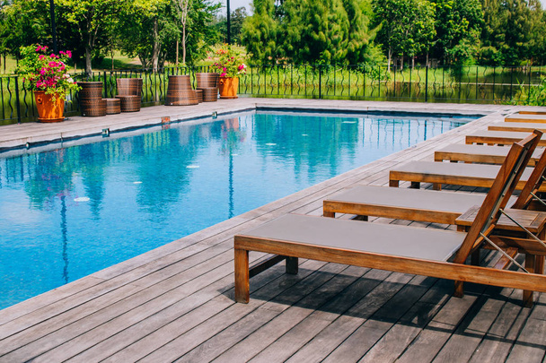 Dřevěné denní místo na dřevěné podlaze vedle bazénu v resortu se zelenou přírodní v pozadí. - Fotografie, Obrázek