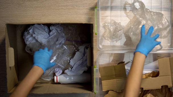 Person in protective gloves separating paper and plastic waste for recycling - Φωτογραφία, εικόνα