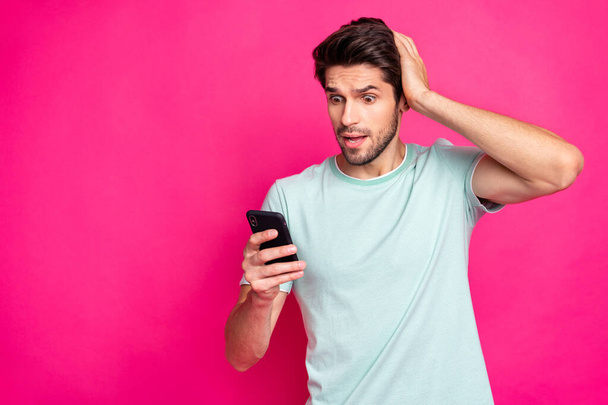 Photo of blogger guy holding telephone in hands checking subscribers noticed many unfollowers wear casual outfit isolated vivid pink color background - Zdjęcie, obraz