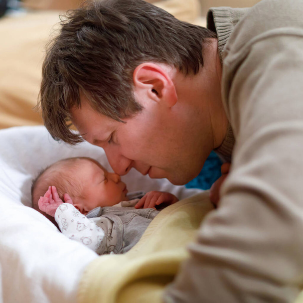Keski-ikäinen isä antaa suukon vastasyntyneelle tyttärelleen. Nuori isä halaa ja halailee tyttövauvaa kotona. Onnellinen vanhemmuus, huoleton lapsuus, perhe, rakkaus. Söpö suloinen vauva nukkuu
. - Valokuva, kuva