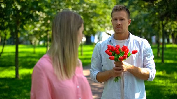 Man in love holding bunch of red tulips for woman, unrequited love, indifference - Фото, изображение