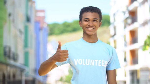 Merry afro-american teenager volunteer showing thumbs-up and smiling on camera - Фото, зображення