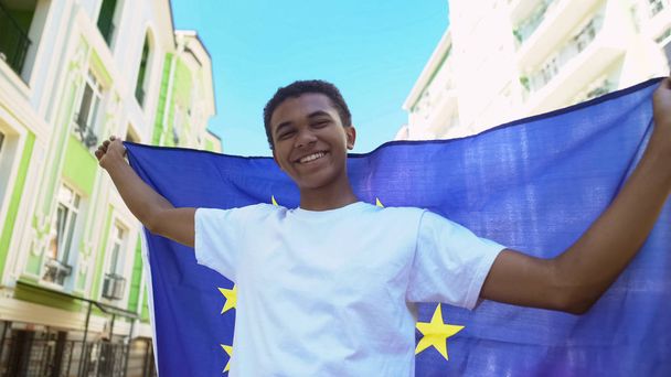 Vrolijke gemengde ras jongeman met vlag van de Europese Unie buiten, vrijheid mars - Foto, afbeelding